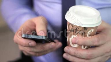 特写男人的手使用手机触摸屏和cofee